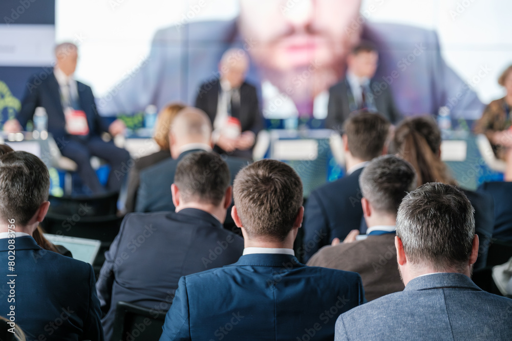 Wall mural Focused audience listening to speaker at a corporate conference event. Business professionals engaged in a dynamic presentation, fostering networking and professional growth.