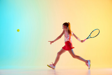 Dynamic shot of teenage girl, tennis athlete training solid cross-court forehand technique in neon...