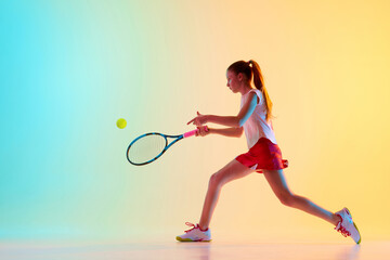 Fit teen girl, tennis athlete trains skills of hitting ball from opponent in neon light against...