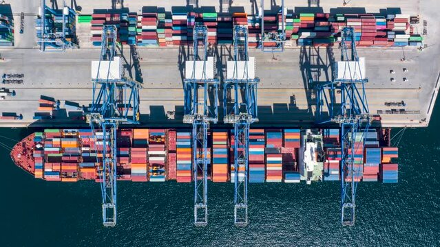Aerial top down time lapse view of  large container cargo ship being unloaded by cranes and trucks in a commercial harbour