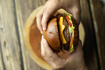 Duas mãos segurando um hamburguer em cima de uma mesa de madeira Two hands holding a burger on a...