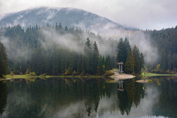 View of Synevyr high-altitude lake by autumn day, Ukraine. The leaf fall forest, lake and mountains. Foggy morning on the lake.