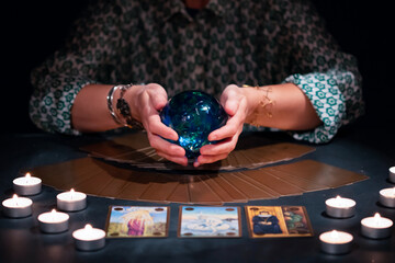 Tarot reader with tarot cards.Tarot cards face down on table near burning candles and crystal ball.