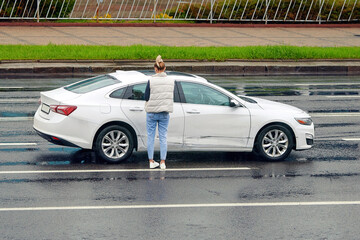 Damaged car on the road after traffic accident, female driver with damaged car. Woman looks at car...