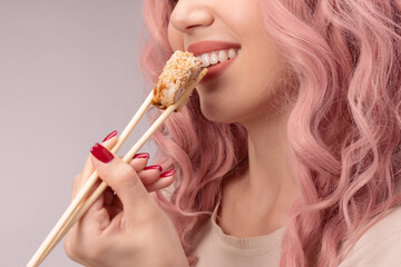 Young woman with red nails and pink hair is eating sushi.