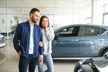 Happy young couple chooses and buying a new car for the family. Visitting the dealership