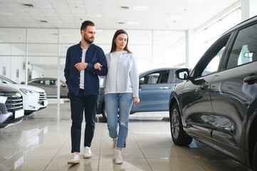 It is the one car I want. Beautiful young couple standing at the dealership choosing the car to buy