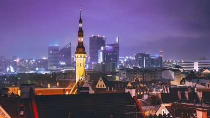 Tallinn, Estonia. Tower Of Town Hall On Background With Modern Urban Skyscrapers. Night City Centre Architecture.