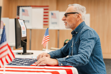 Elderly gray haired man, voter wearing eyeglasses sitting at polling station talking, registering