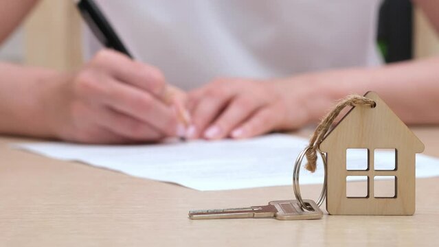 House keys on the table, blurred female hands signing mortgage loan agreement on background. Insurance, buying home, real estate concept. Selective focus