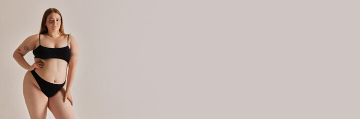 Obraz premium Beautiful young girl with oversized, plus size body posing in underwear against grey studio background. Concept of natural beauty, body positivity, care, acceptance. Banner. Empty space to insert text