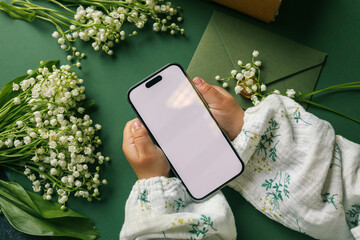 Phone in hands with isolated screen on the background of lilies of the valley