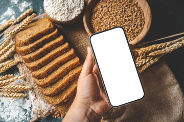 Phone in hand with isolated screen on background of bread, ears of corn and flour, bakery products