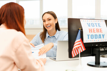 Beautiful, happy woman, worker working at polling station, talking to voter, holding ballot paper