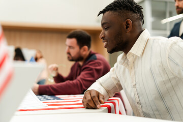 Happy African American man, US citizen, sitting at registration table decorated with American flag