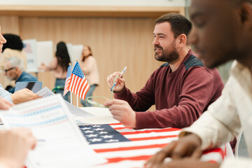 Smiling Caucasian man, US citizen, sitting at registration table decorated with American flag
