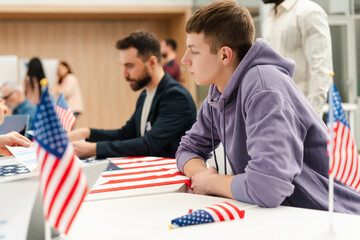 Attractive young man, voter sitting at registration table at polling station, with American flags