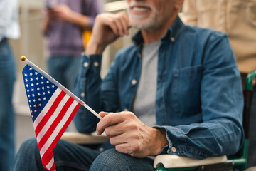 Elderly male voter sitting in wheelchair holding American flag, selective focus standing in line