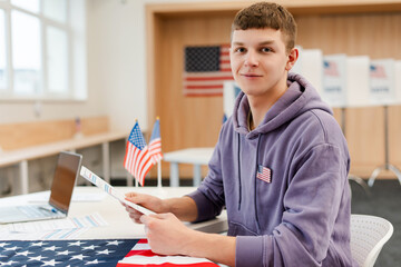 Portrait of smiling handsome young man voter sitting at registration table at polling station