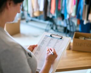 Close Up Of Female Charity Worker With Clipboard Checking Donations At Foodbank Or Thrift Store