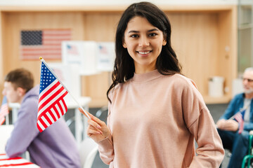 Portrait of smiling attractive Asian woman American citizen holding American flag, looking at camera