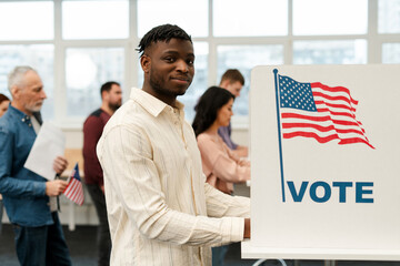 Attractive smiling African American man voter standing in election booth voting looking at camera