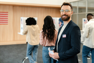Middle aged, smiling man, voter wearing stylish eyeglasses standing in line at polling station