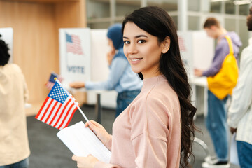 Happy Asian woman, American citizen holding American flag and ballot paper standing in line to vote