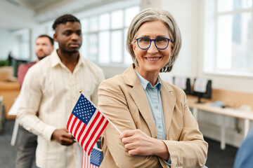 Happy senior woman wearing stylish eyeglasses holding American flag looking at camera in line