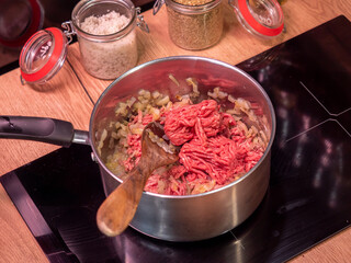minced meat in a metal pot on a hot stove with a wooden spoon inside