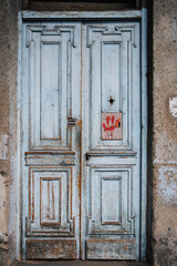 Old wooden door with peeling paint, and a red smiley painted on it of dilapidated house in Kala, Tbilisi Old town, Georgia