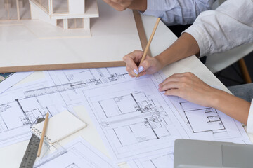 Professional engineer measures house model while skilled designer writes down in blueprint. Work...