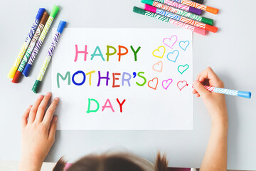 child draws with multi-colored felt-tip pens a poster gift card for mom with the inscription text Happy Mother's Day, holiday concept