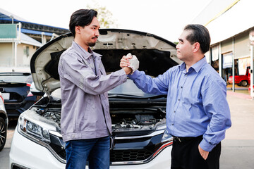 Japanese mechanic car shaking hands with an Asian customer with an opened radiator hood car. Focus...