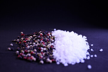 Peppercorns and coarse salt on a black background scattered on the surface