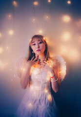 Portrait of a beautiful Asian woman with angelic wings, wearing white clothes and illuminated by the glow of a garland, exuding beauty and elegance.