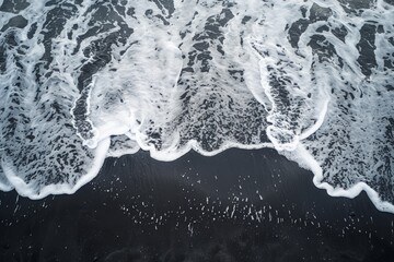 High-angle view of the ocean waves gently washing over a vast stretch of black sand beach - Powered by Adobe