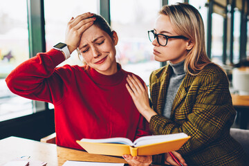 Depressed student crying because of difficulties in learning of studying material from textbook during private lesson with qualified female tutor.Teacher helps stressed hipster girl after fail in test