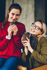 Portrait of two pretty young women holding tasty coffee to go enjoying free time in stylish...