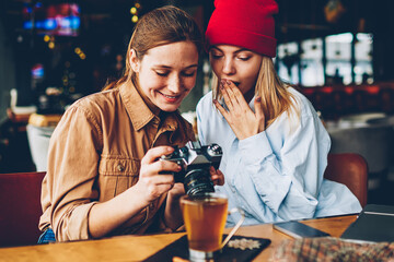 Wondered stylish teenager with cheerful friend female photographer dressed in casual outfit...