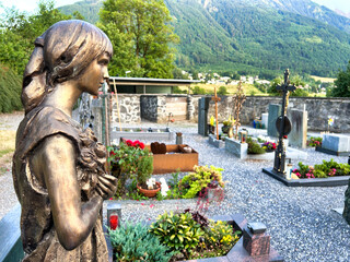 A statue of a woman holding a flower is in front of a cemetery