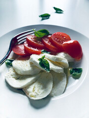 Classica insalata caprese italiana con mozzarella fresca a fette, pomodori, foglie di basilico e olio d'oliva in un piatto bianco. Piatto estivo. Concetto di cibo italiano. Direttamente sopra.