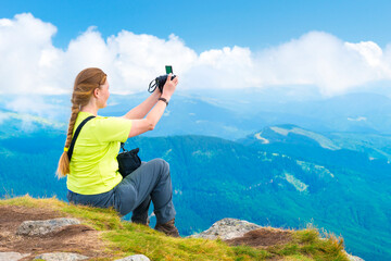 Young woman sitting on mountain cliff and taking travel selfie