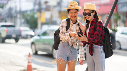 Obraz premium Two young Asian female tourist friends reading a tourist map on their mobile phone on the street in Thailand.