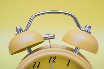 Close up of yellow alarm clock on yellow background, vintage color tone