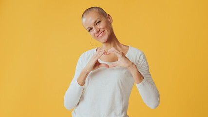 Young hairless woman showing representing heart in shape of fingers gesture, looking at camera...