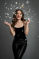 Studio portrait of young beautiful happy woman in black outfit against gray background.