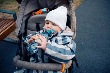 Cute boy drinks water from a bottle while sitting in a baby carriage stroller