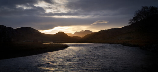 The River Gruinard at sunrise with the distant sun drench summits of Beinn Dearg Bheag and Beinn Dearg Mor in the Scottish Highlands, Scotland in the UK.