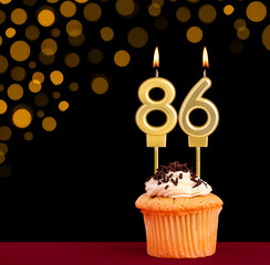 Number 86 birthday candle - Cupcake on black background with out of focus lights